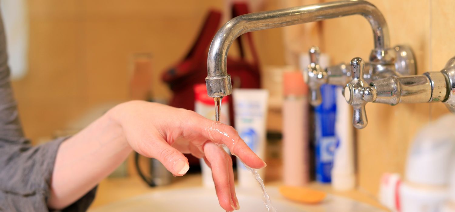 Hand testing low water pressure from a bathroom faucet, illustrating common well pressure tank and water pressure issues.
