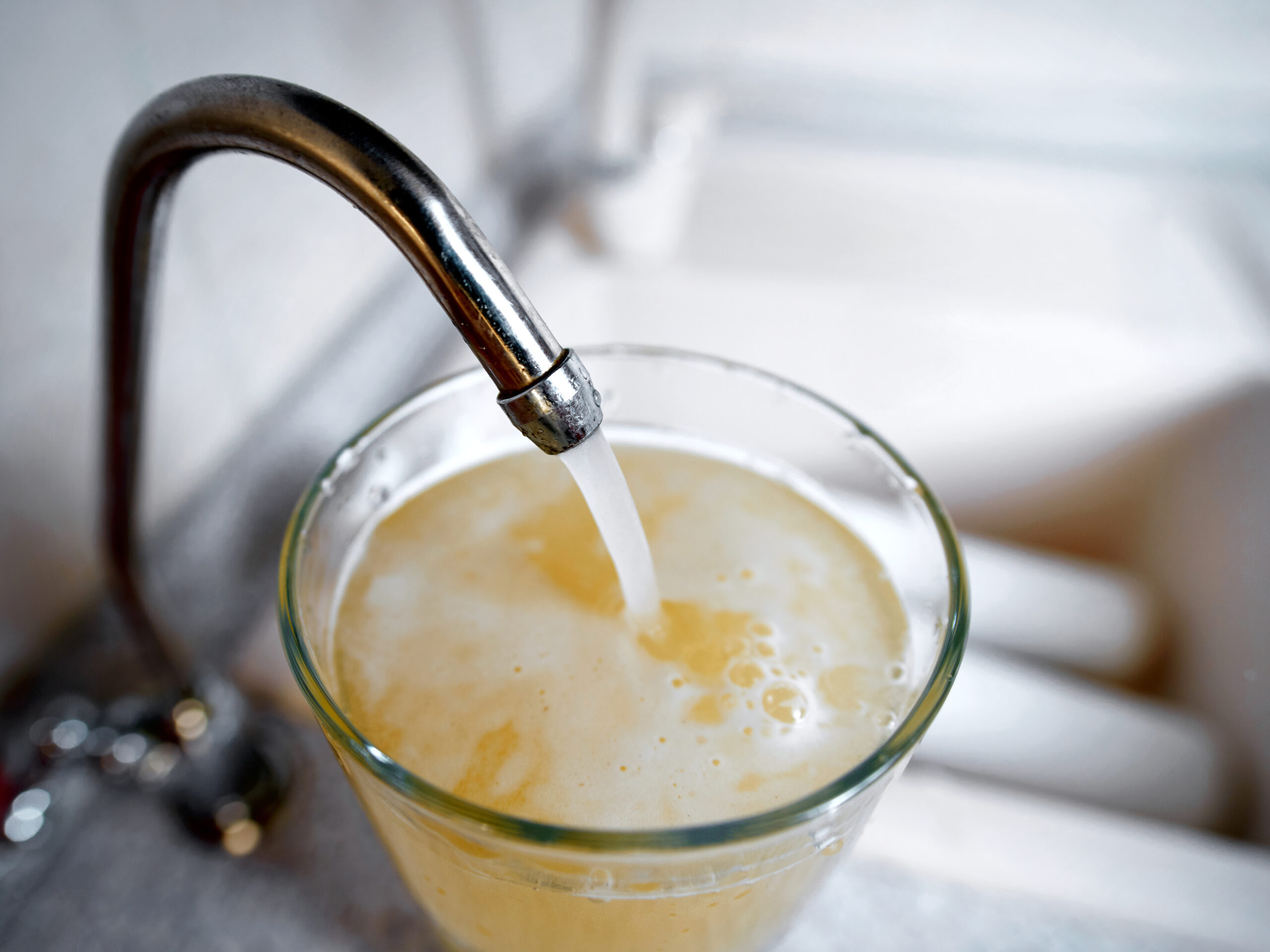 A glass being filled from a faucet with cloudy, discolored water, indicating potential contamination or well issues.